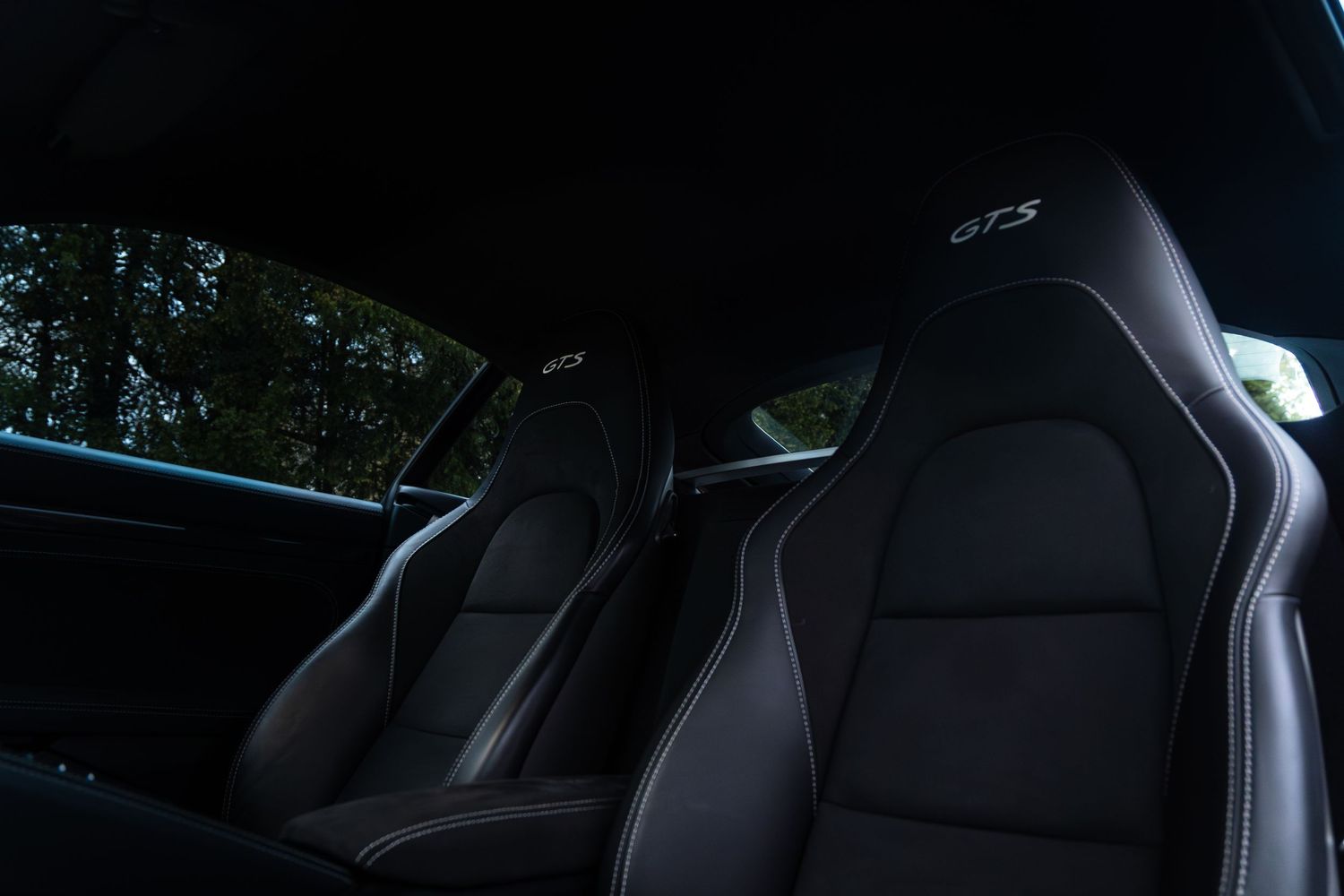 Dark interior shot of Porsche 718 Cayman GTS twin black sport seats with GTS embroidery detail.