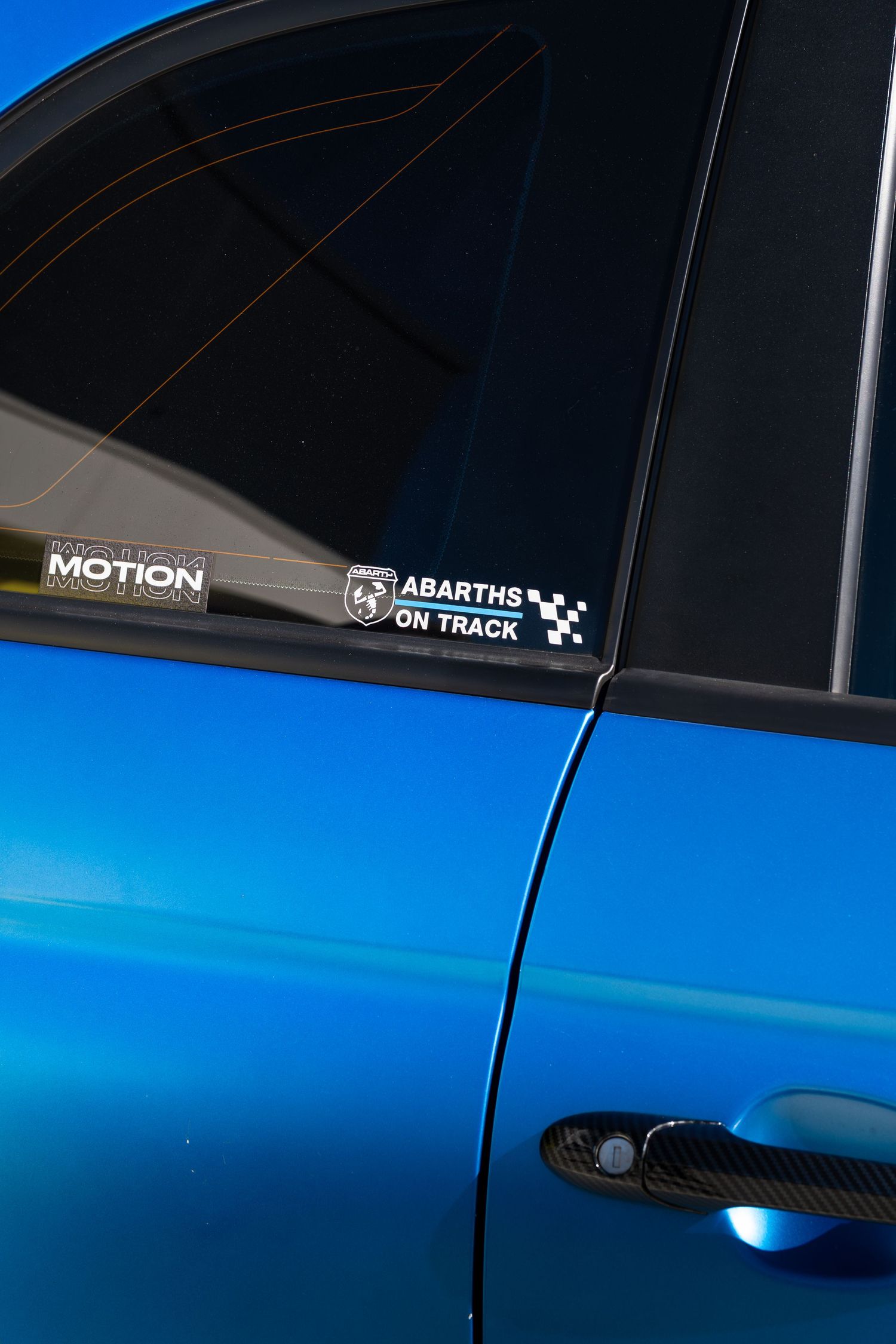Close-up of a blue Abarth door pillar showing Motion and Abarths on Track sticker decals.