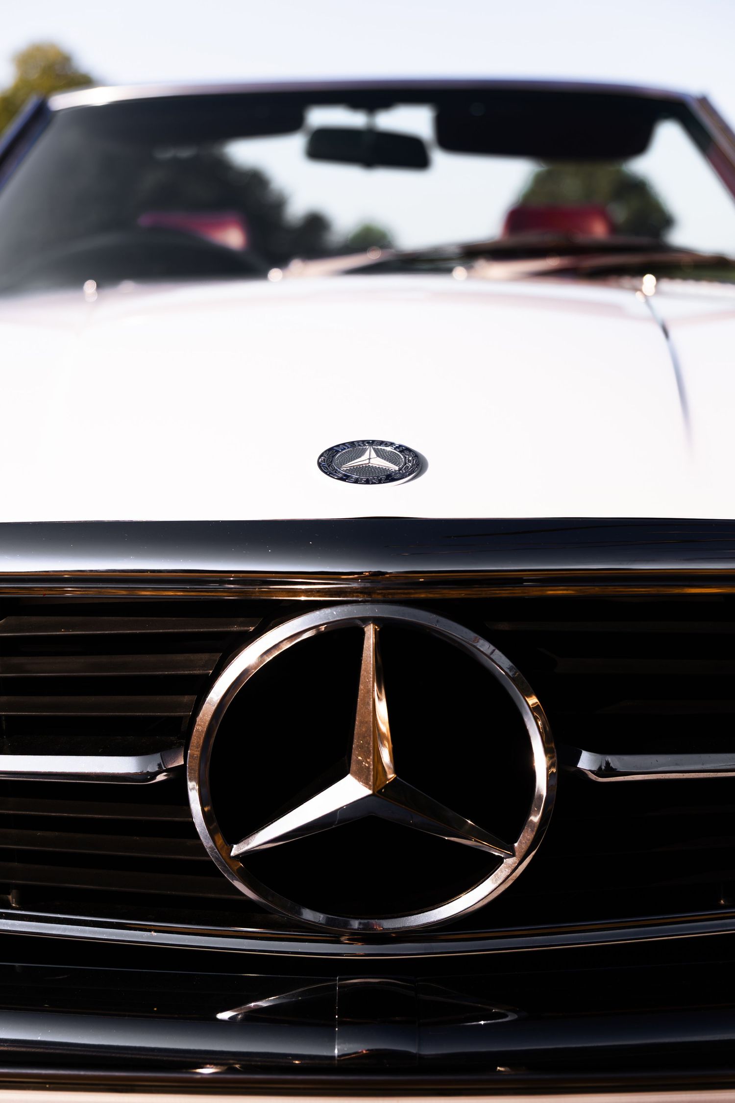 Close-up of a chrome Mercedes-Benz three-pointed star logo on the front grille of a white convertible car.