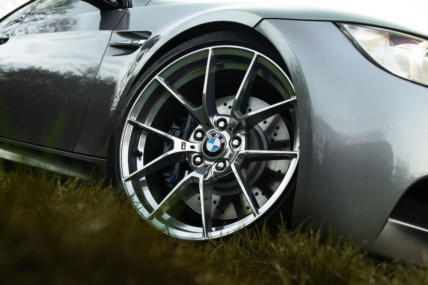 BMW M3 front alloy wheel with blue brake caliper and BMW roundel on grass.