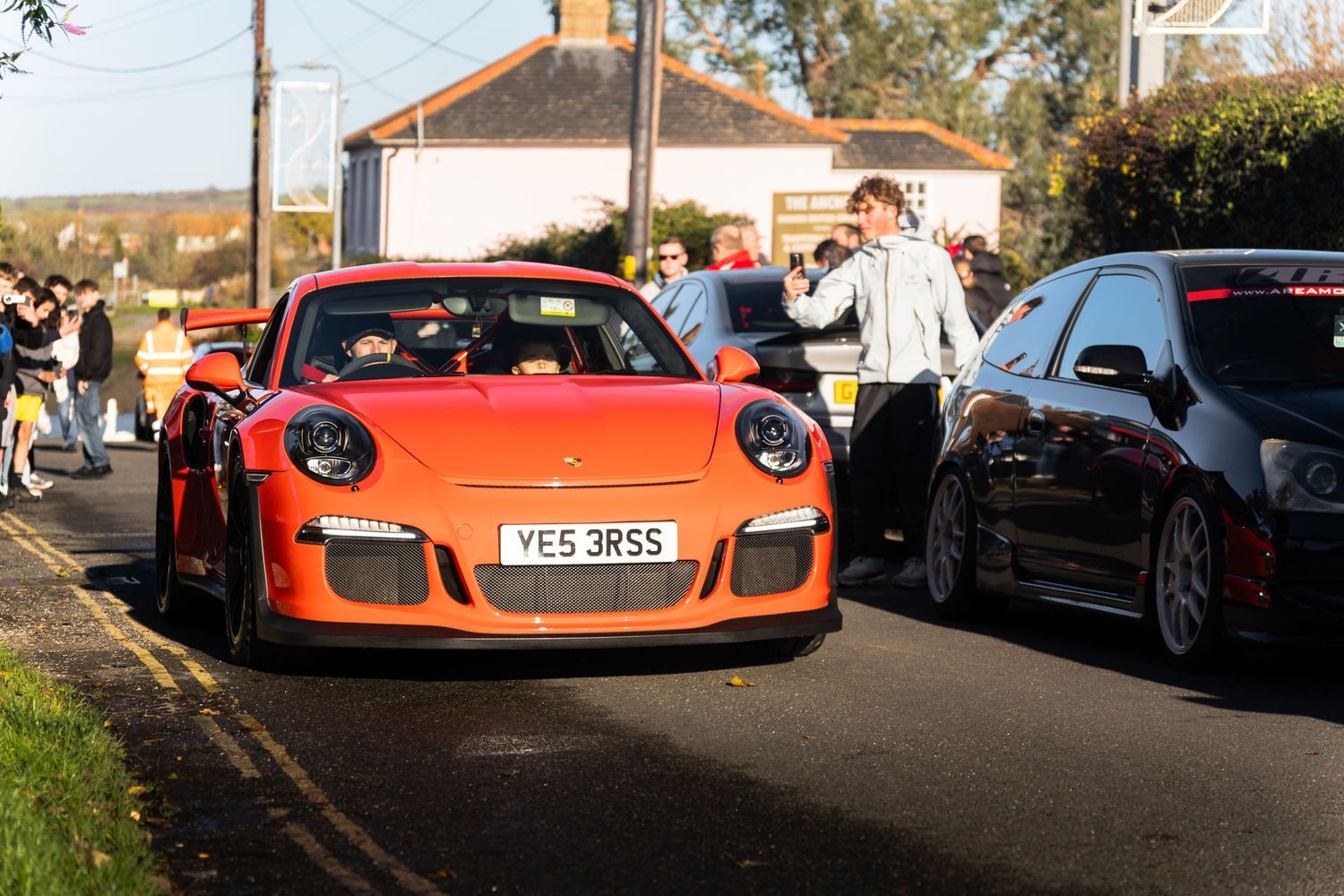 Orange Porsche 911 GT3 RS with personalized plate surrounded by crowds at a UK car meet.