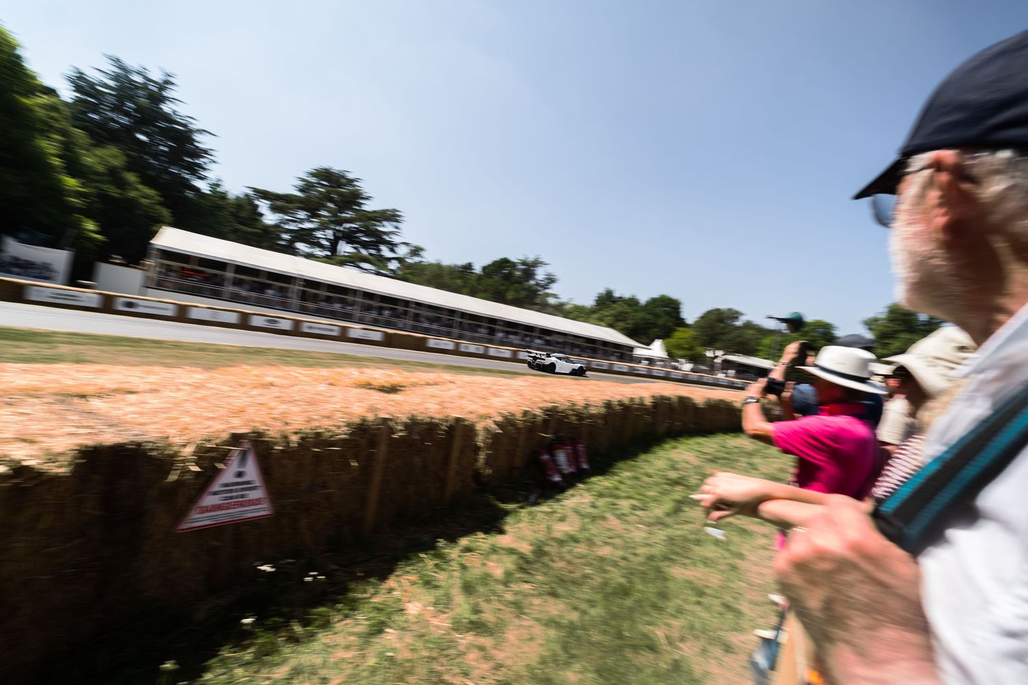 Spectators watch racing cars on a track at Goodwood Festival of Speed on a sunny summer day.