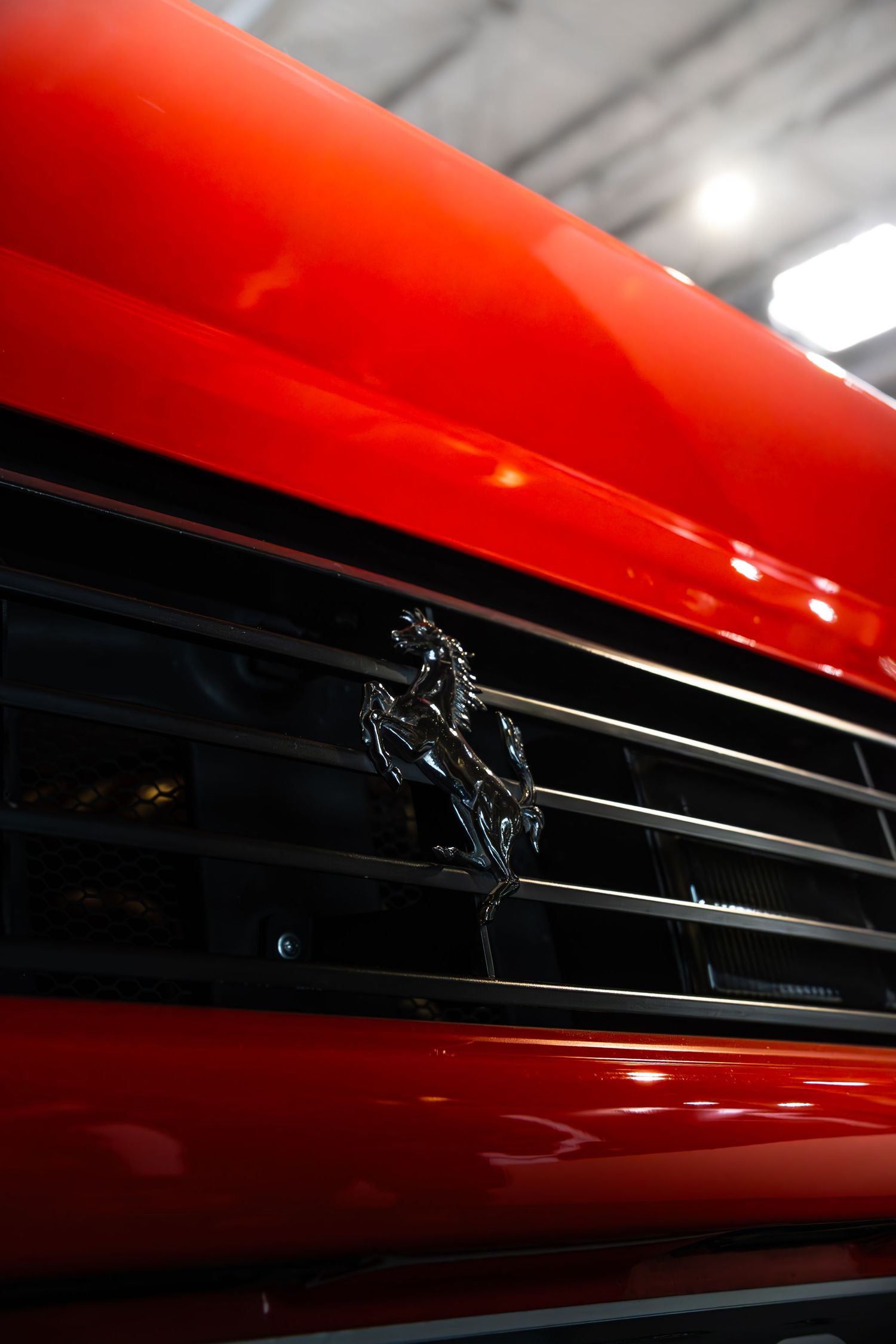 Close-up of black prancing horse Ferrari logo on red car front grille at auto show.