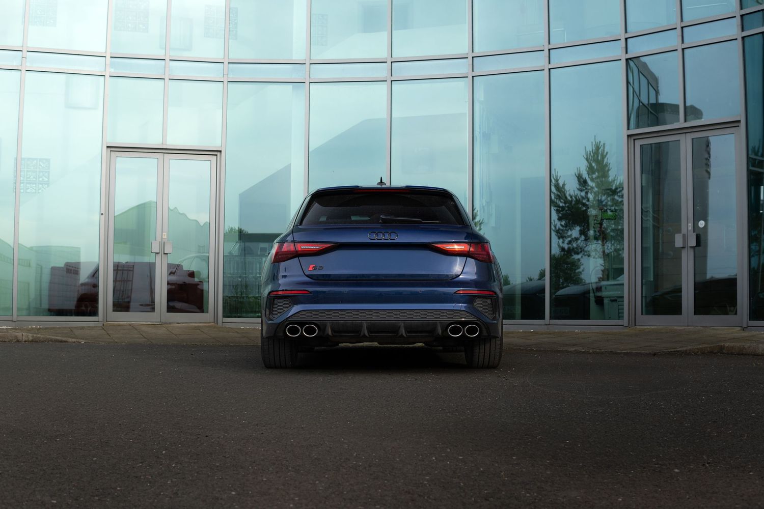 Rear view of a blue Audi RS Q3 parked in front of a modern glass building facade.