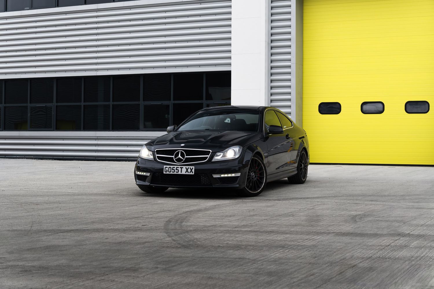 Black Mercedes-AMG C63 coupe positioned at three-quarter angle near yellow industrial garage doors.