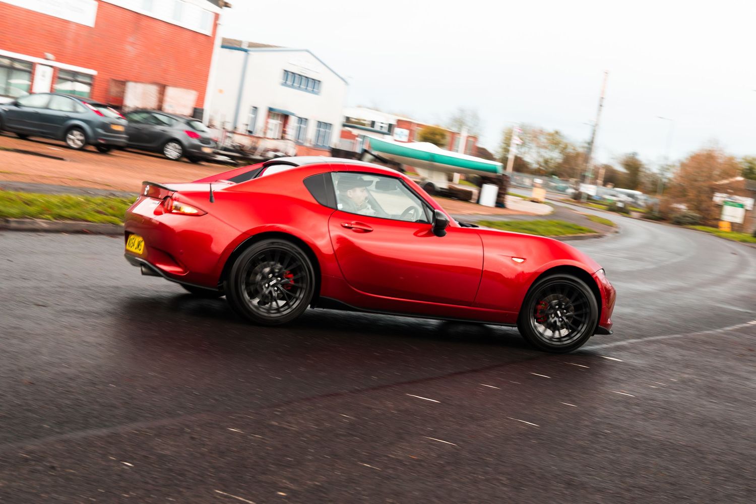 Red Mazda MX-5 RF hardtop convertible driving on wet UK road on an overcast day.