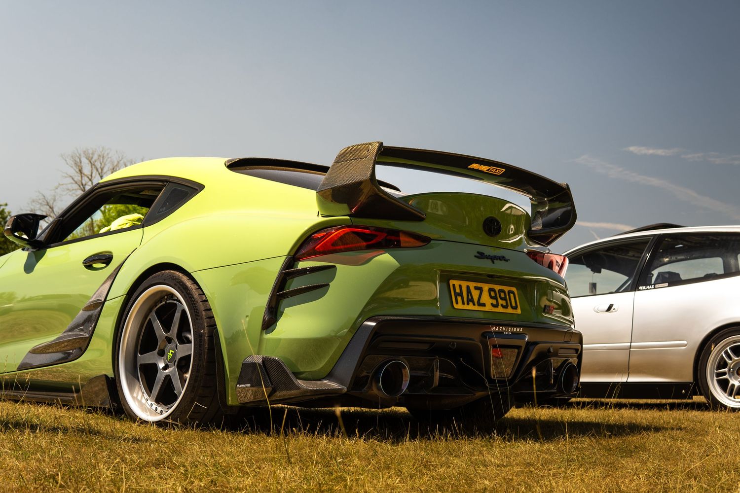 Lime green Toyota Supra A90 with carbon fiber rear diffuser and large wing spoiler at a car meet.
