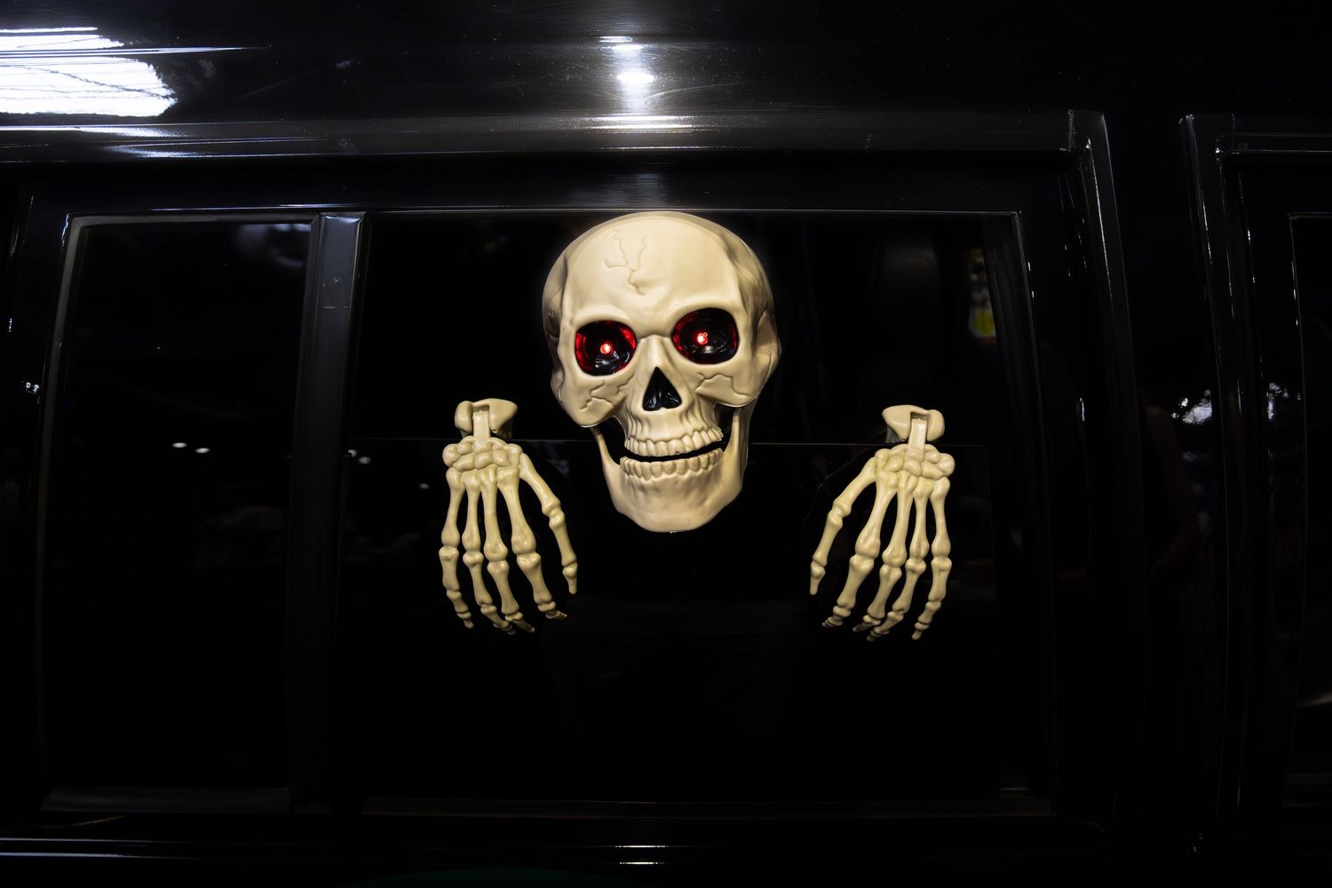 Halloween skeleton decoration with glowing red eyes displayed inside dark car window.