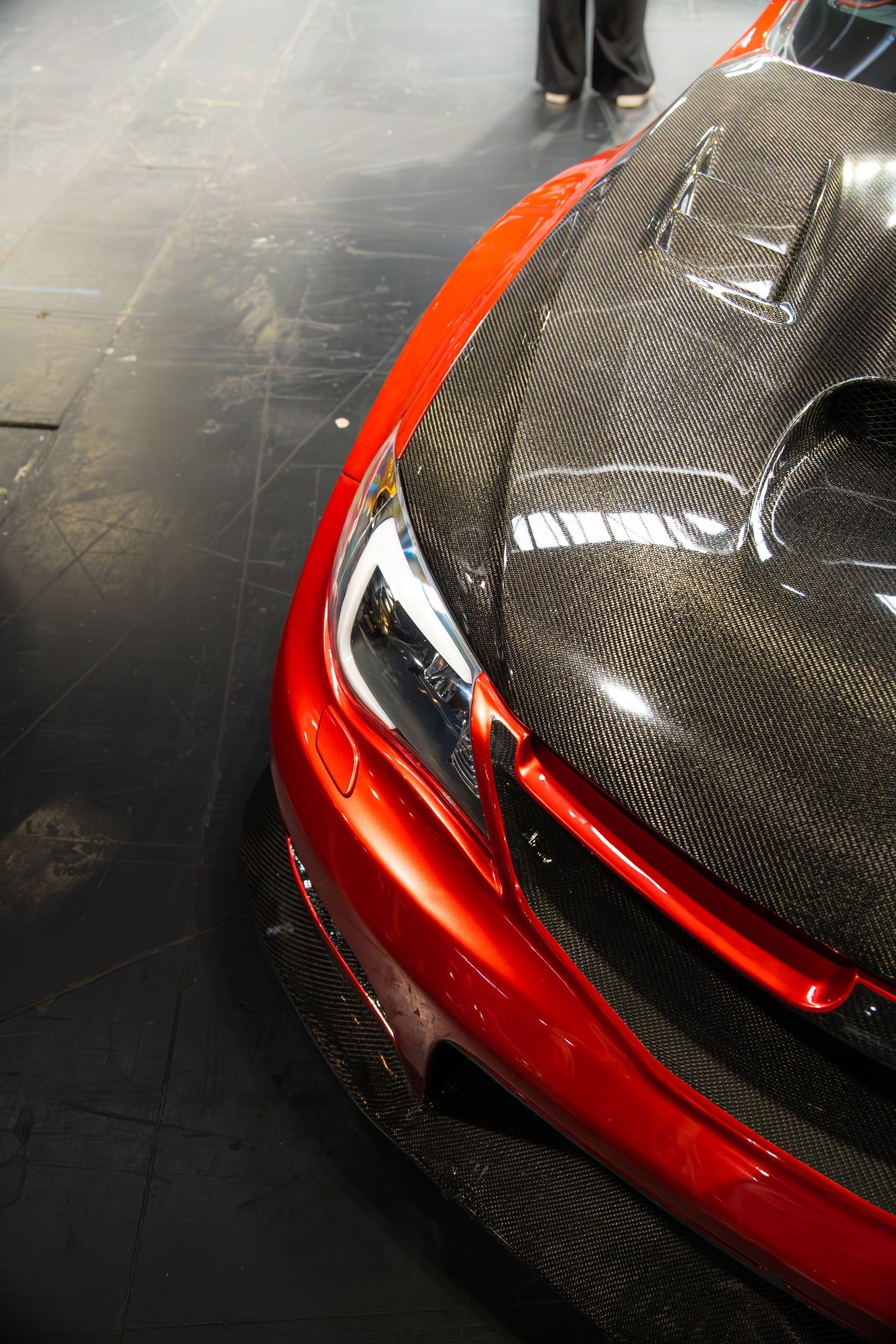 Close-up of red car with carbon fiber hood and front bumper splitter at auto show.