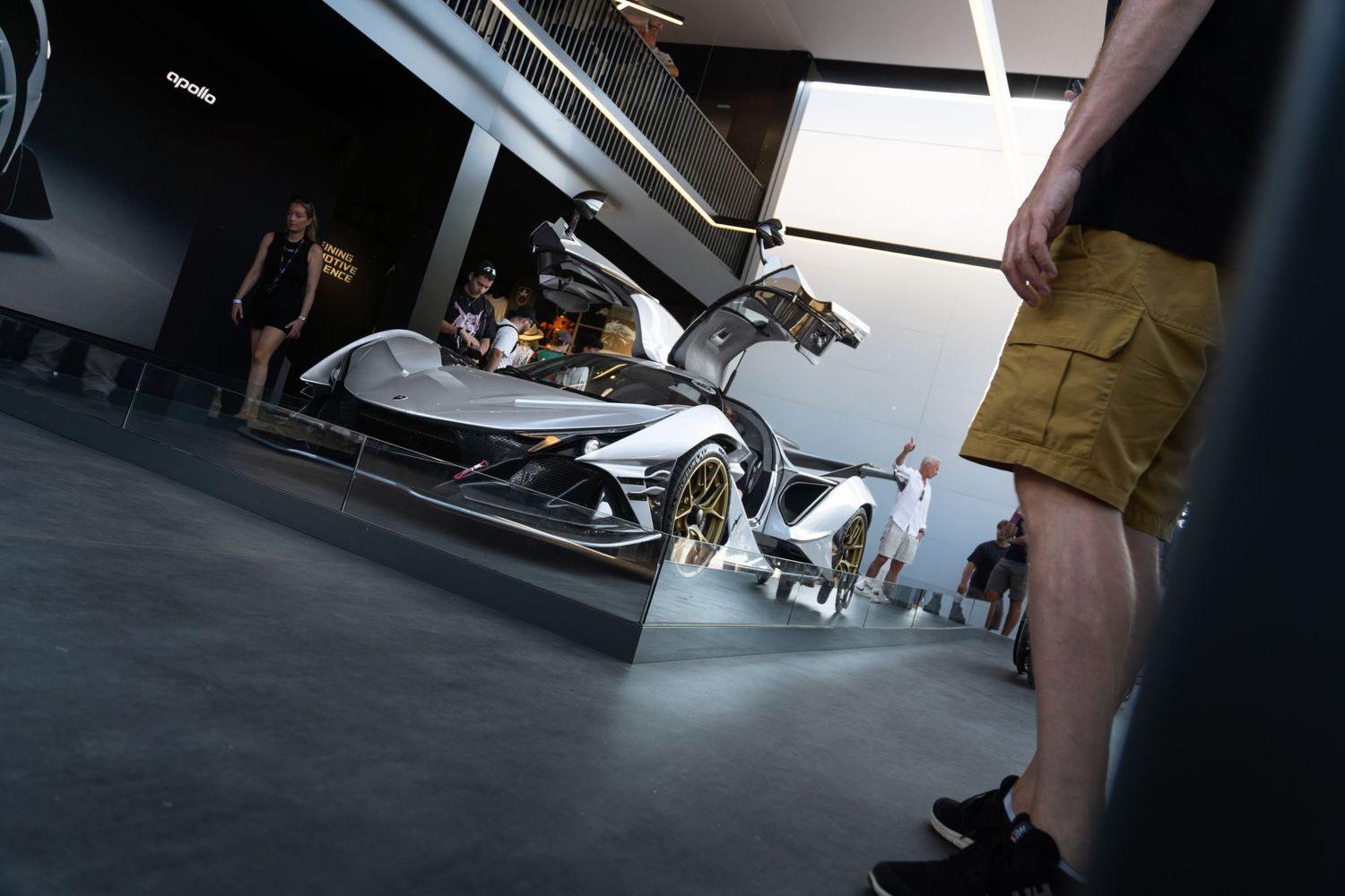 Visitors admire a sleek white concept supercar on display at a modern automotive exhibition.