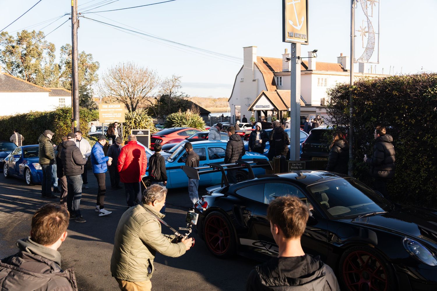 Crowd of car enthusiasts gathered around exotic cars at an outdoor automotive event.
