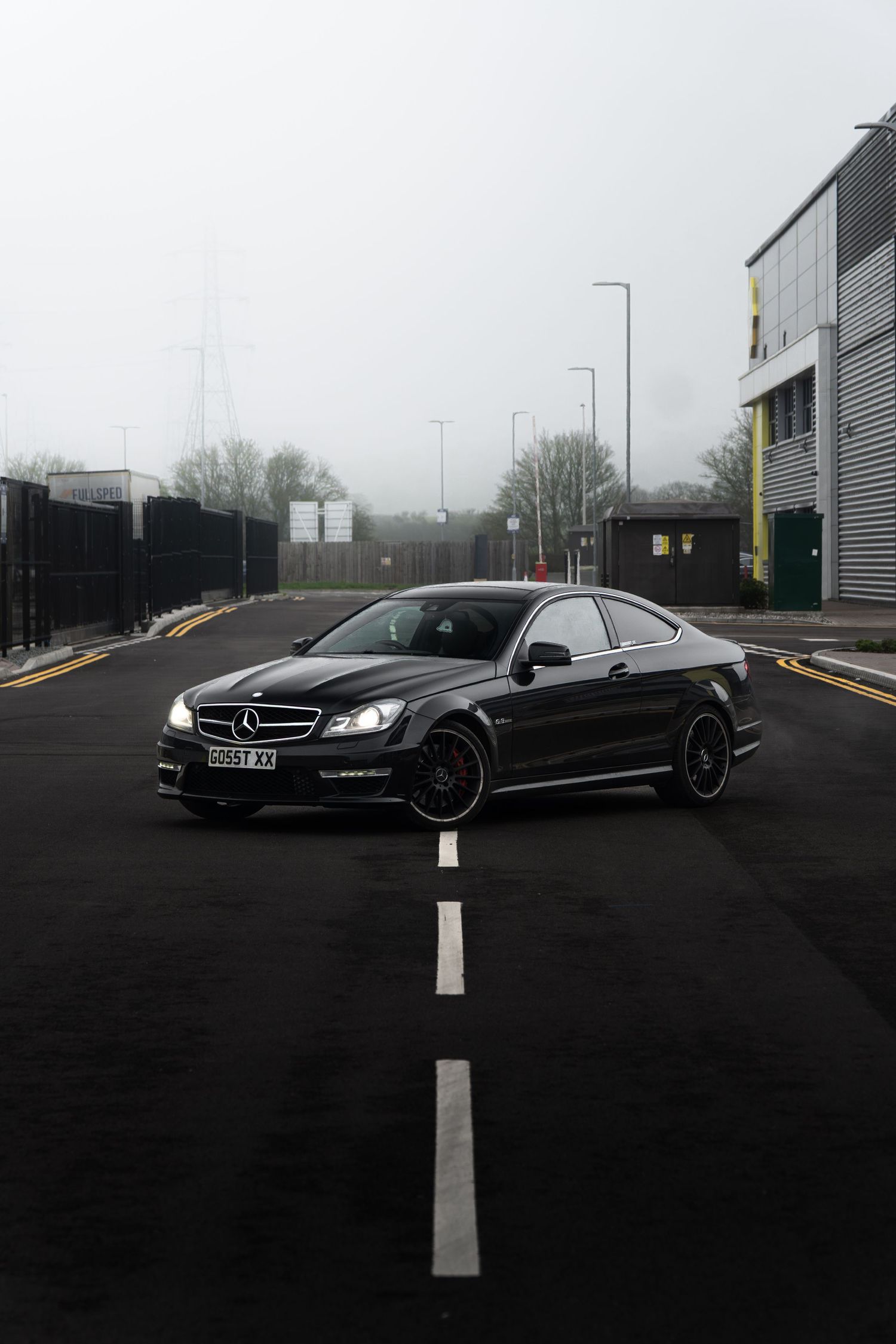 Black Mercedes-Benz C63 AMG coupe centered on road markings in overcast weather.