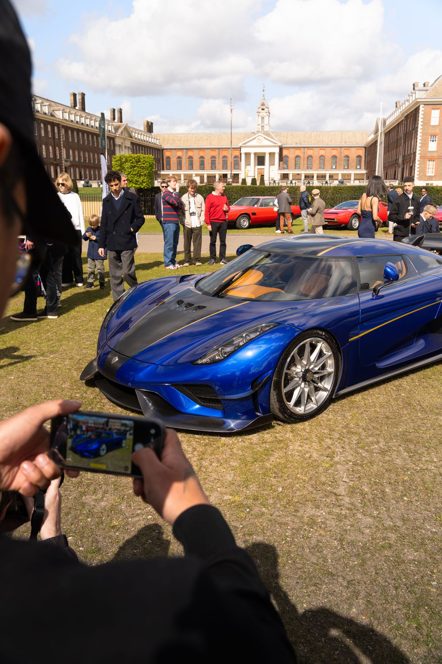 Blue Koenigsegg Regera supercar being photographed by spectators at an outdoor car show.