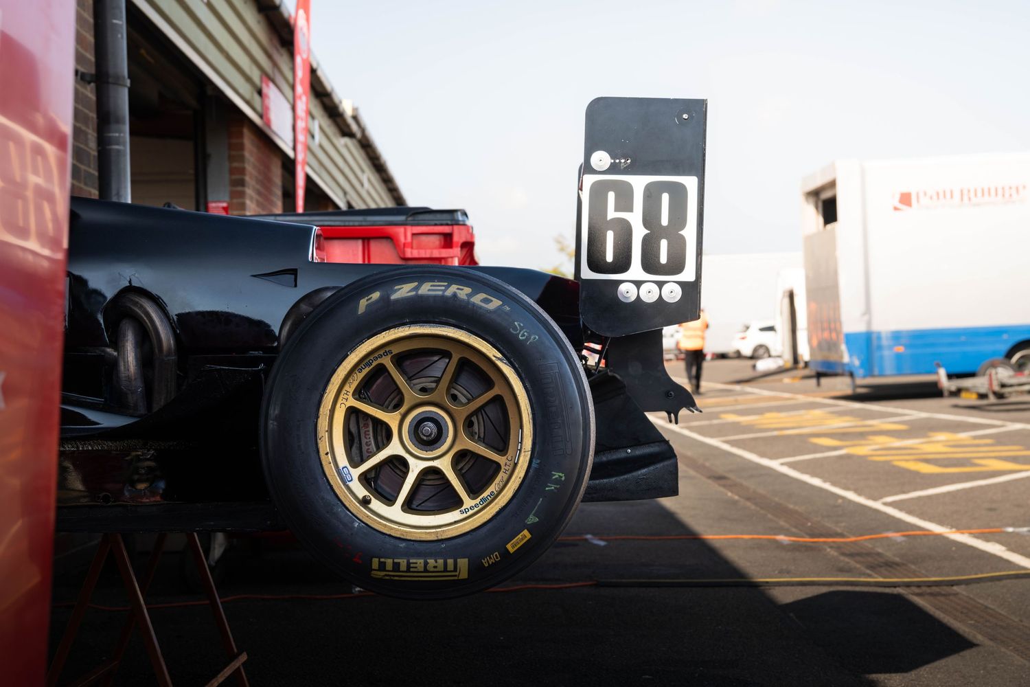 Pirelli P Zero gold alloy wheel on racing car number 68 in pit lane at motorsport event.