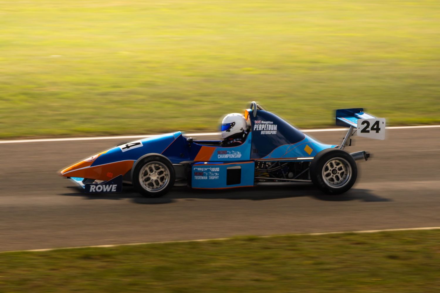 Blue Formula racing car number 24 with ROWE sponsorship speeding on sunny race track.
