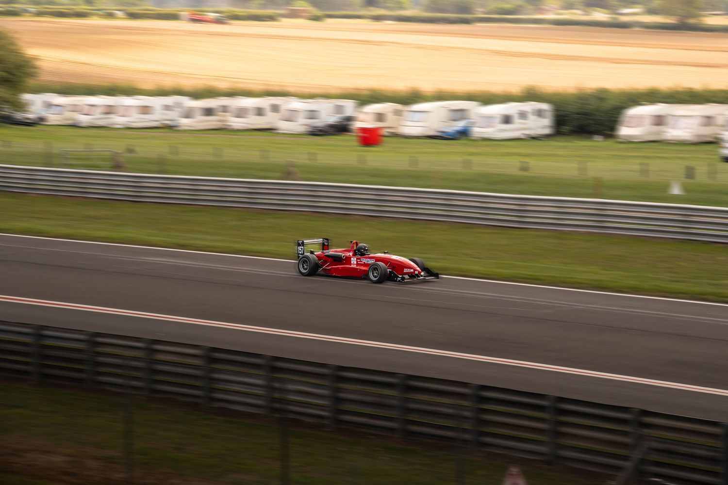 Red open-wheel formula racing car speeding along a circuit straight.
