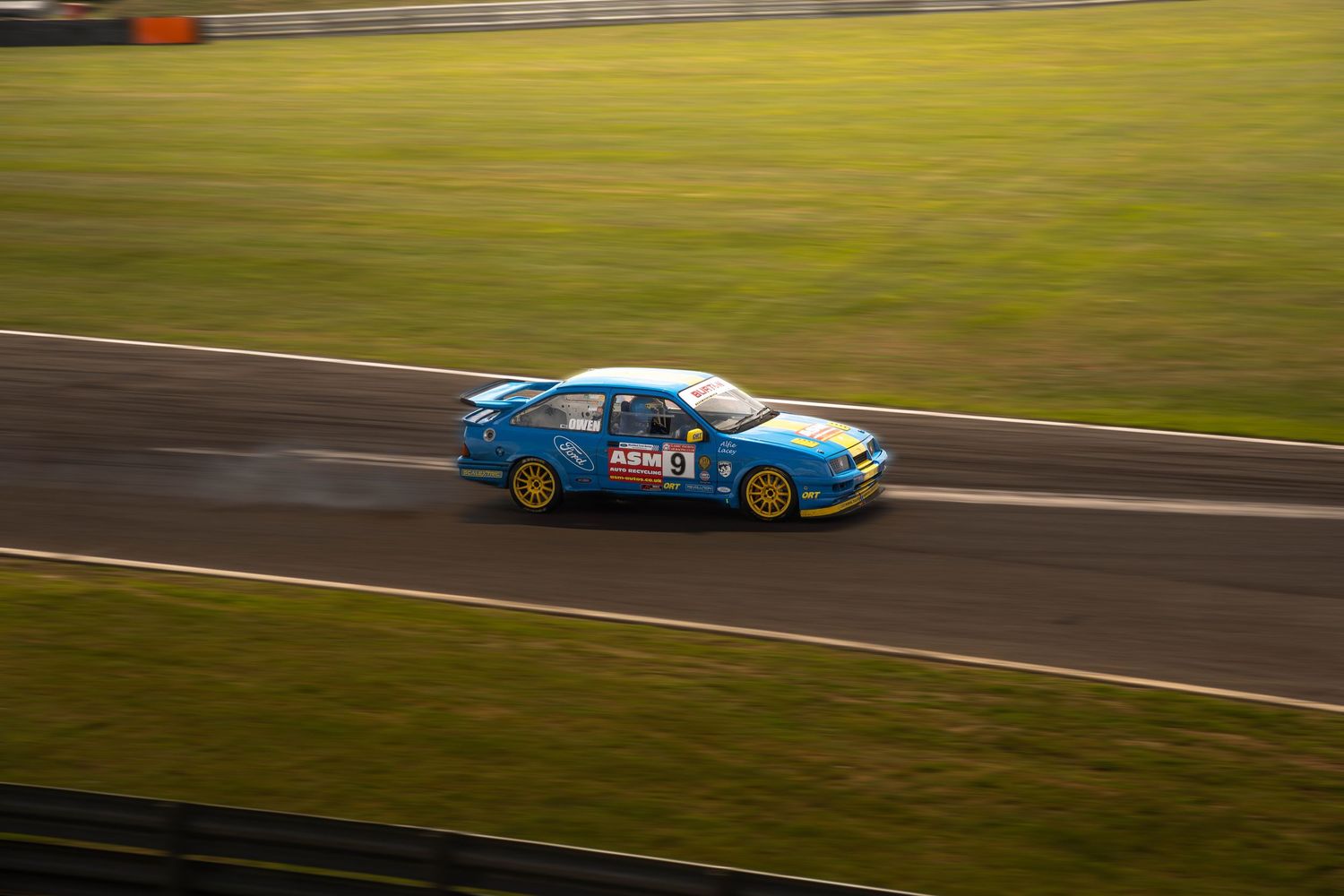 Blue Ford Sierra racing car speeding along a motorsport circuit track.