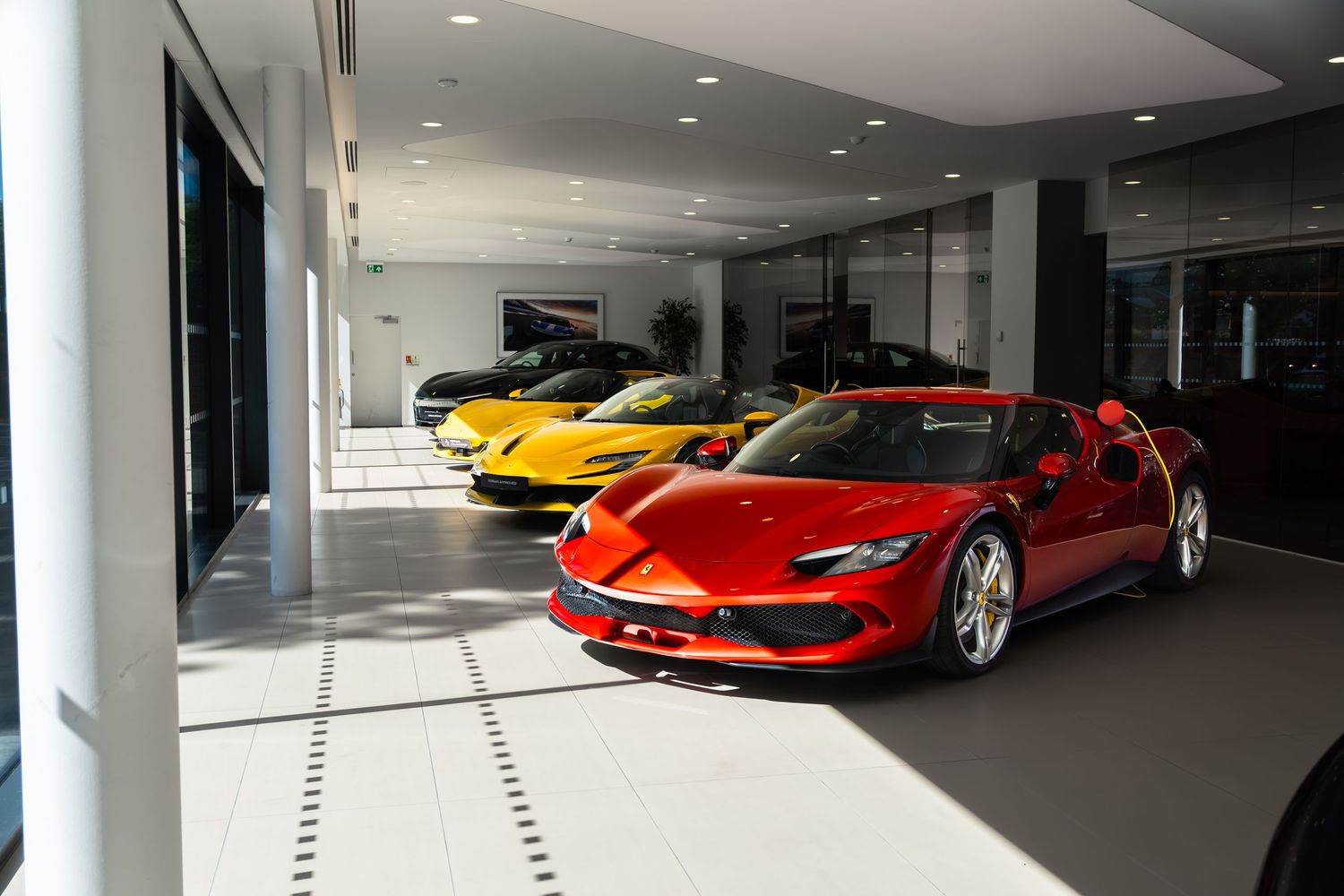 Luxury Ferrari sports cars displayed in a modern showroom, featuring a red Ferrari 296 GTB and yellow models.