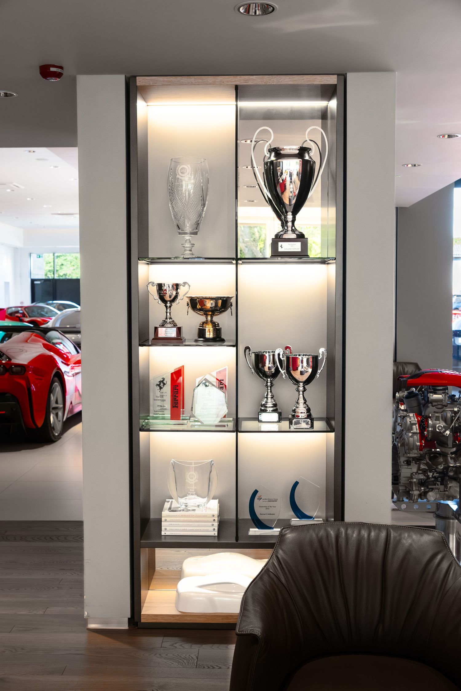 Illuminated display cabinet showcasing Ferrari racing trophies and awards in a luxury car dealership showroom.