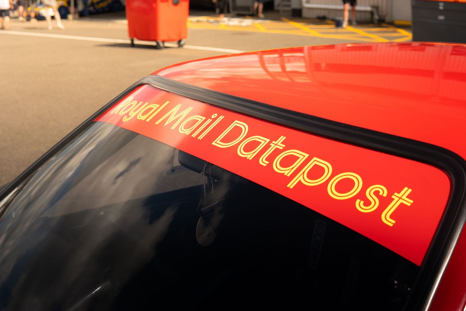 Red Royal Mail Datapost sponsored race car windscreen banner at motorsport paddock.