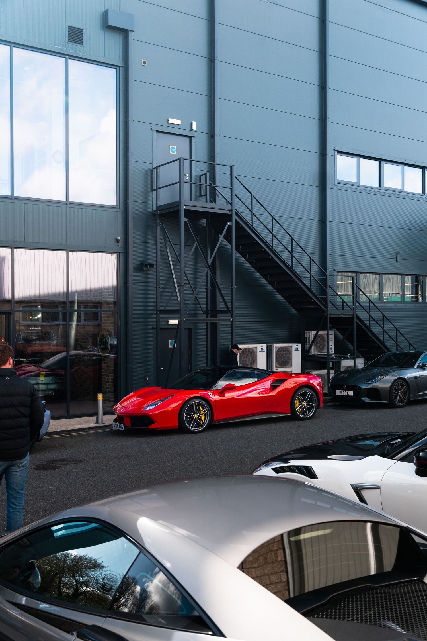 Red Ferrari 488 parked outside a modern grey industrial building with metal staircase.