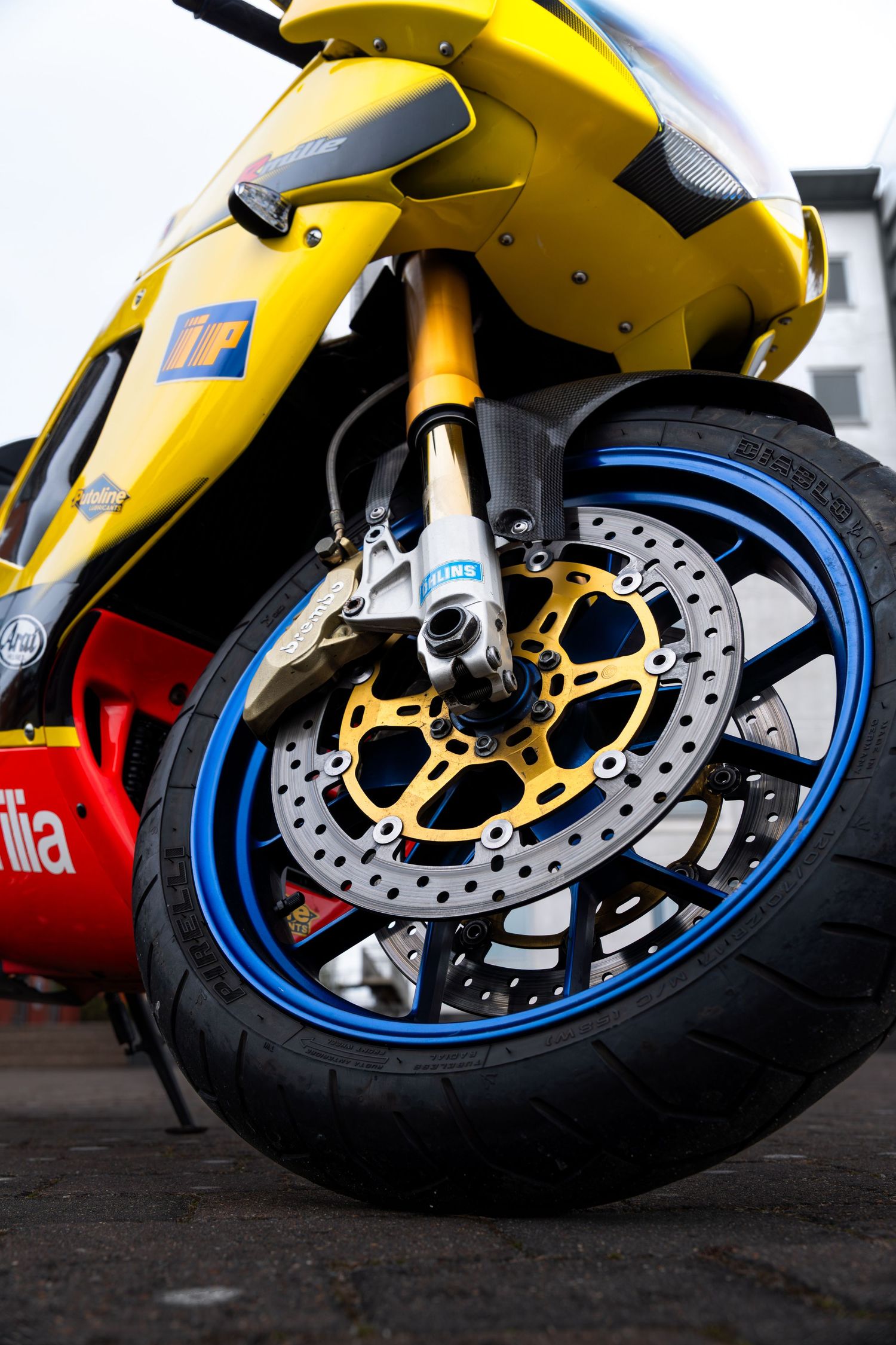 Close-up of Aprilia RSV-R front wheel with gold brake disc, blue rim, and Ohlins gold fork suspension.