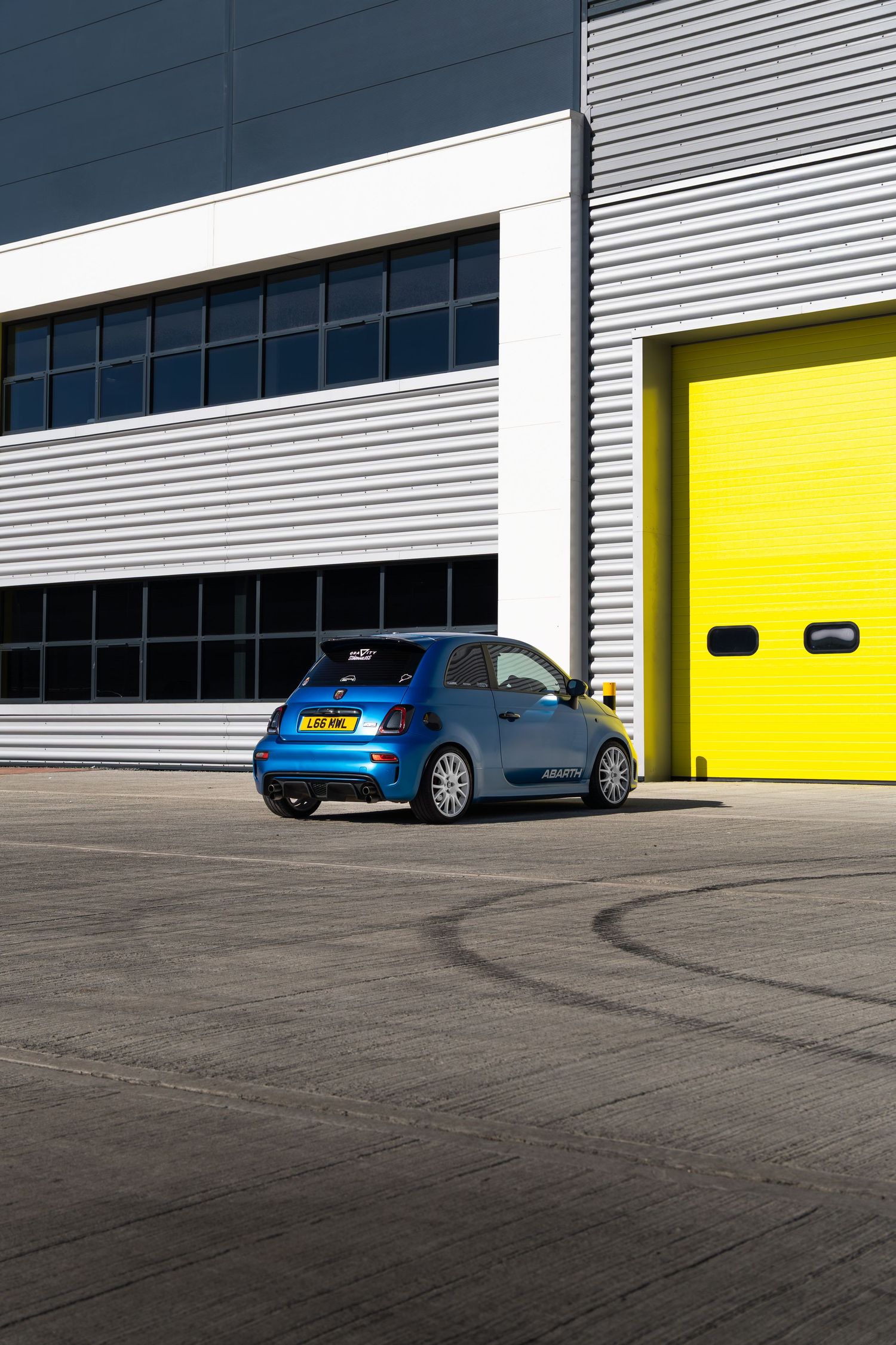 Blue Abarth 500 rear view parked outside industrial building with yellow roller door.