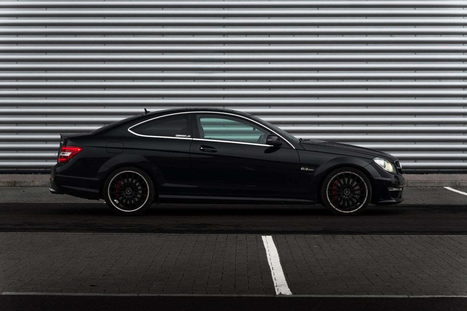 Black Mercedes-AMG C63 coupe in perfect side profile against a corrugated metal wall backdrop.