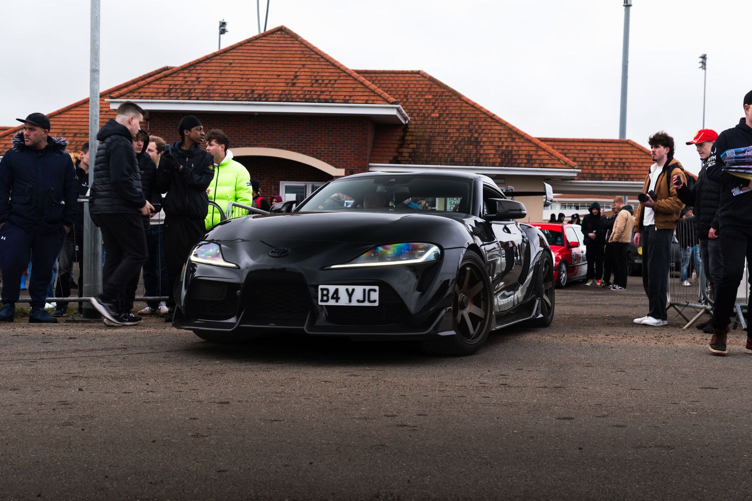 Matte black Toyota GR Supra A90 at a car show event with spectators in background.