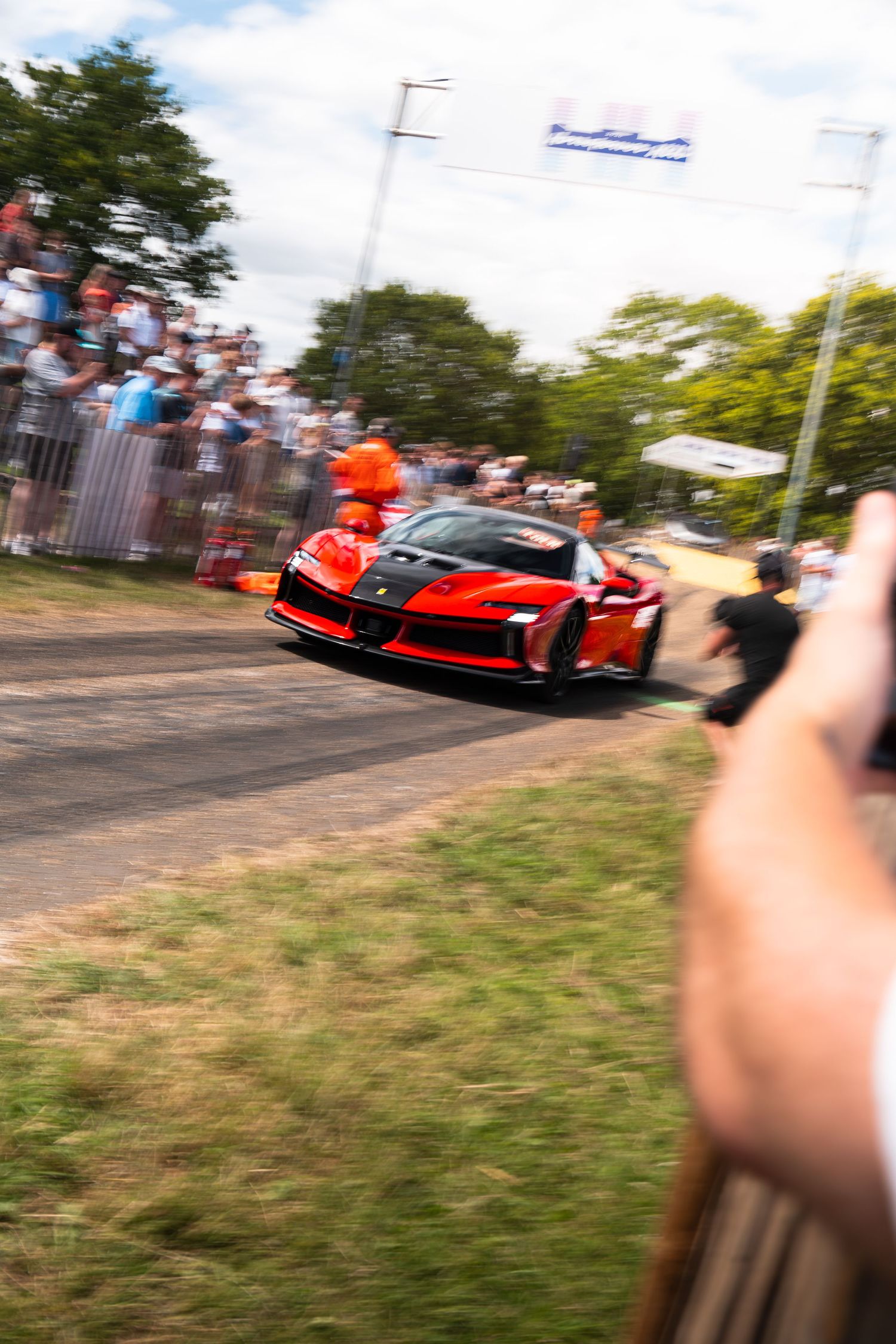 Red Ferrari supercar racing at Goodwood Festival of Speed with spectators watching from barriers.