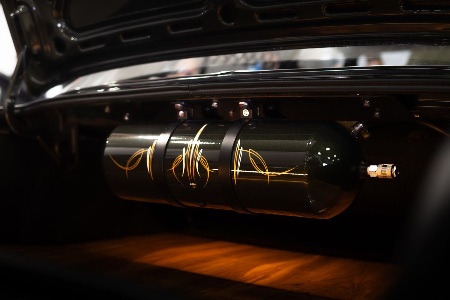 Custom nitrous oxide bottle with gold flame graphics mounted in a car display window.