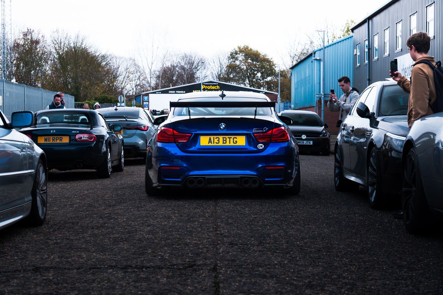 Rear view of a blue BMW M4 with a spoiler at an outdoor car meet.
