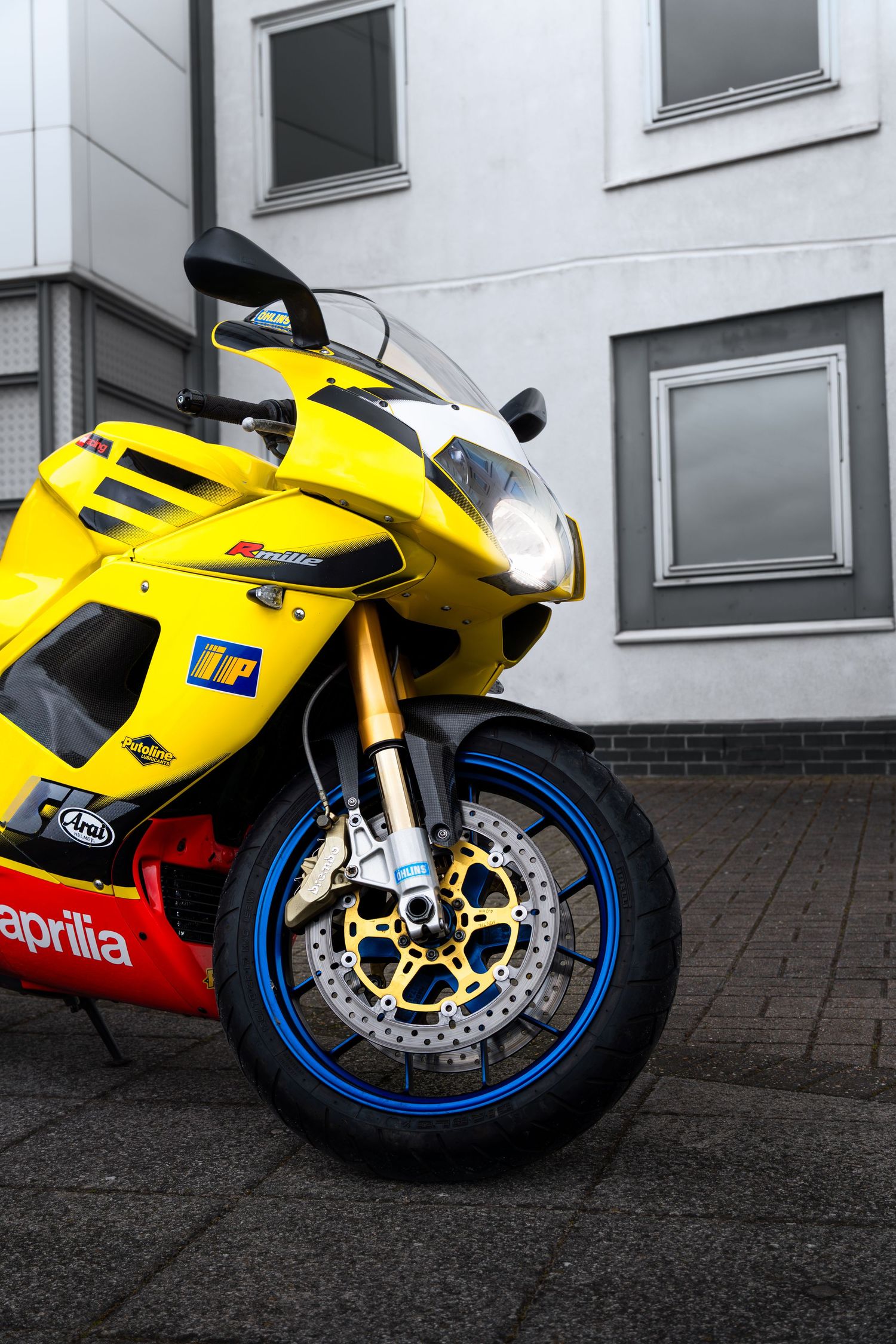 Close-up front view of a yellow Aprilia RSV1000 showing blue-rimmed wheel and gold brake discs.