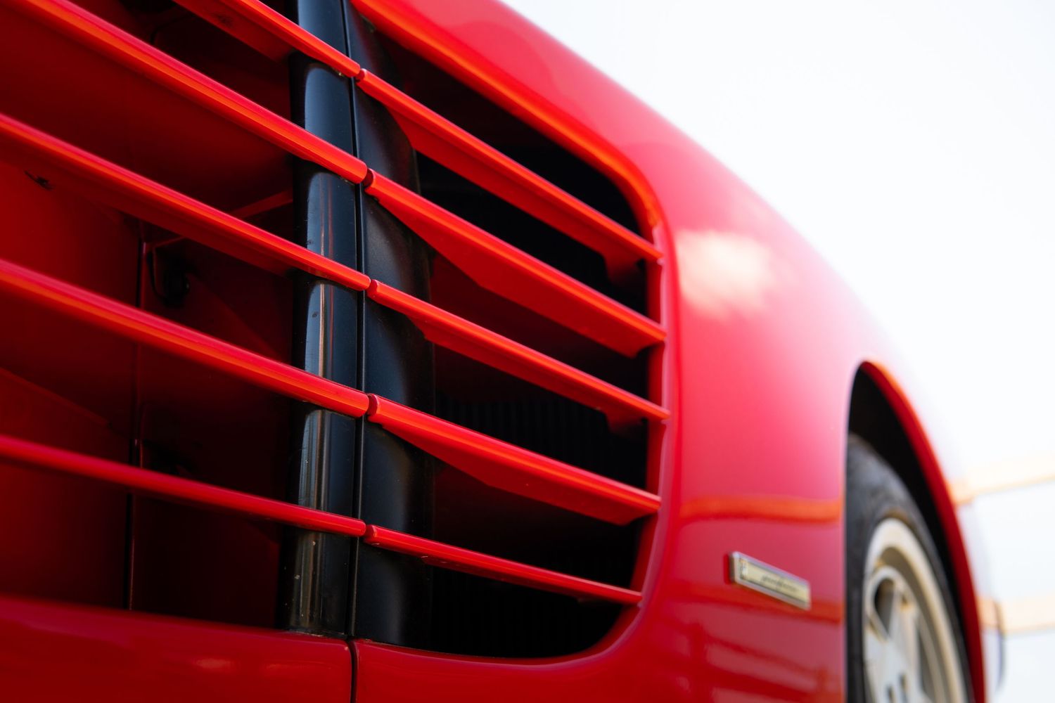 Close-up detail of red Ferrari engine vents and side intake louvers in bright sunlight.