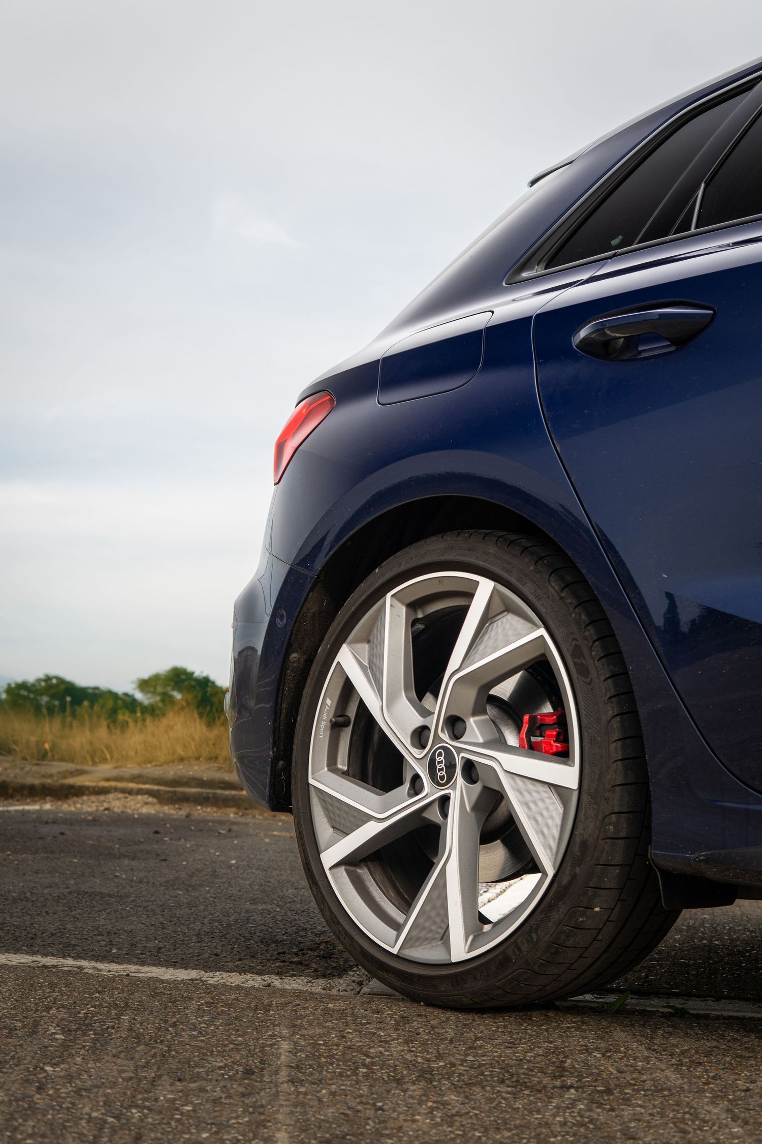 Rear quarter view of a navy blue Audi S3 with red brake calipers on a open road.