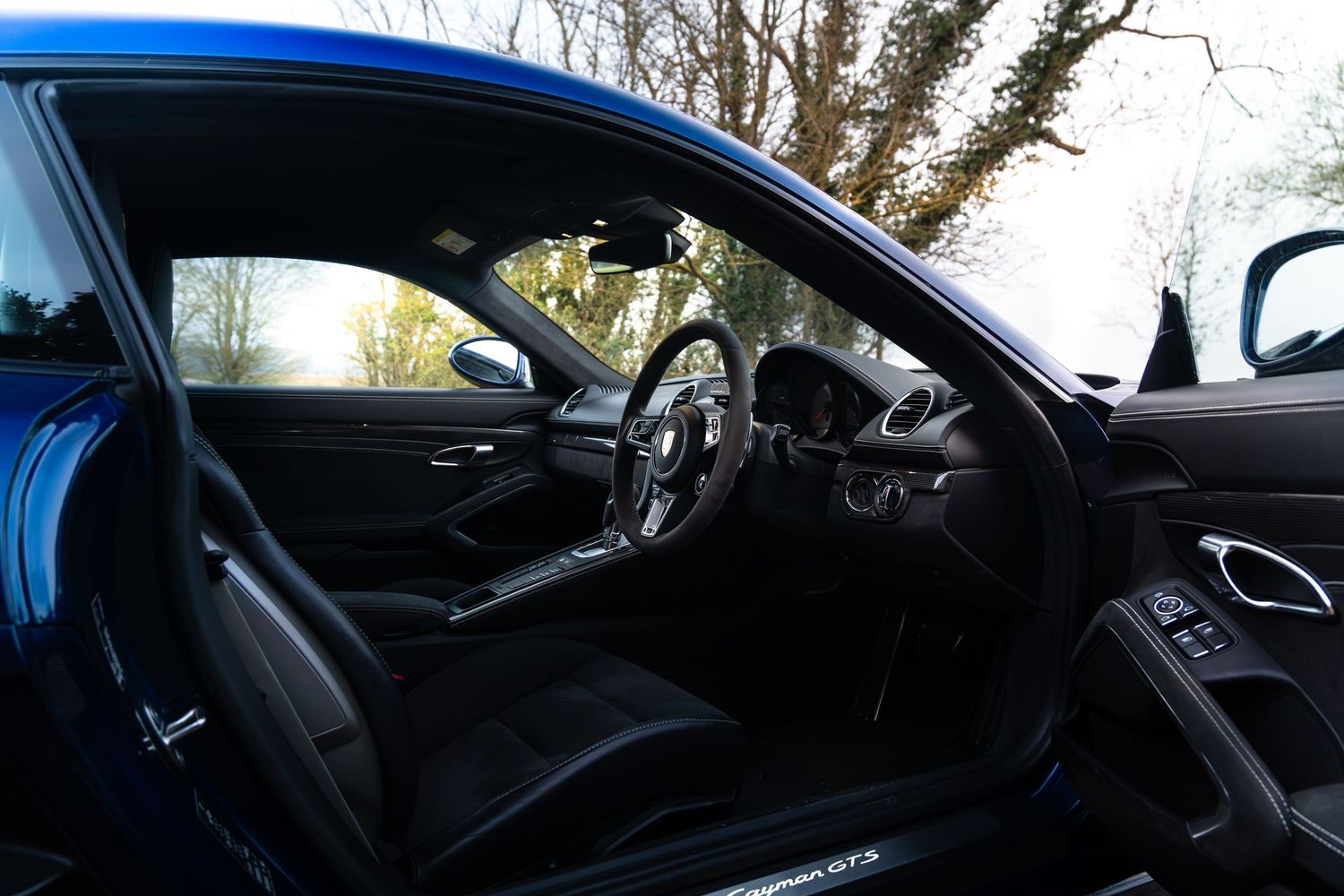 Porsche Cayman GTS interior viewed through open door showing sport seats and center console.