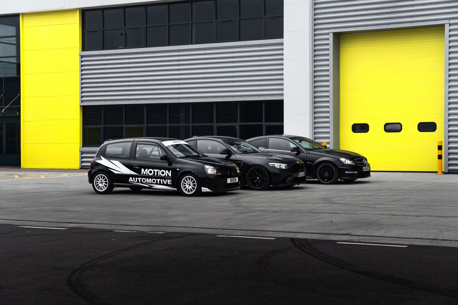 Three black Motion Automotive vehicles lined up outside an industrial building with yellow garage doors.