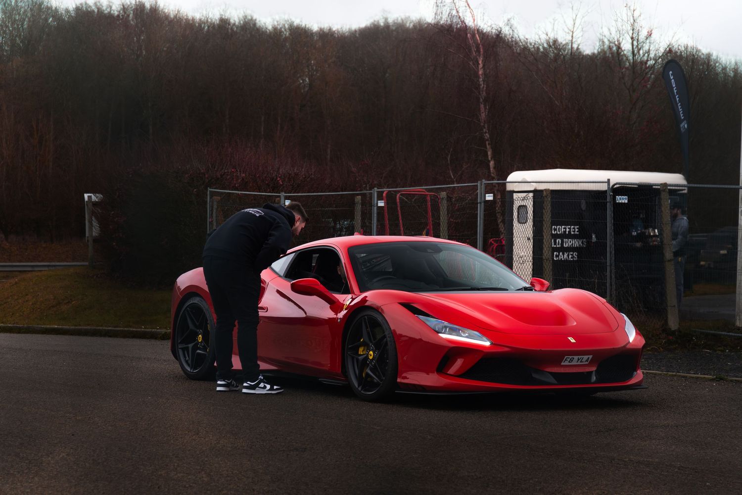 Red Ferrari F8 Tributo supercar parked in lot with person standing nearby.