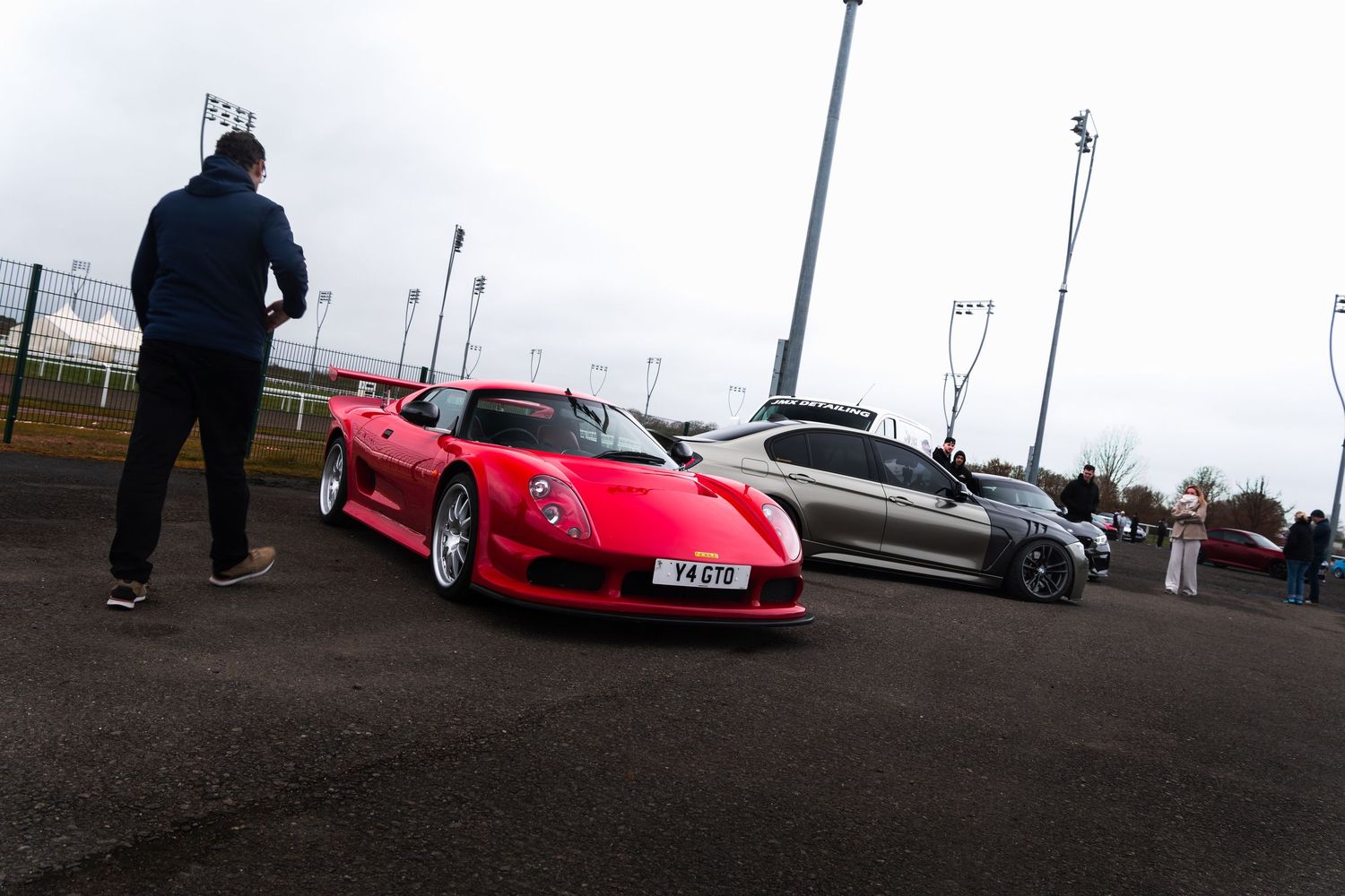 Red Noble M12 GTO supercar on display at an outdoor automotive enthusiast meet event.