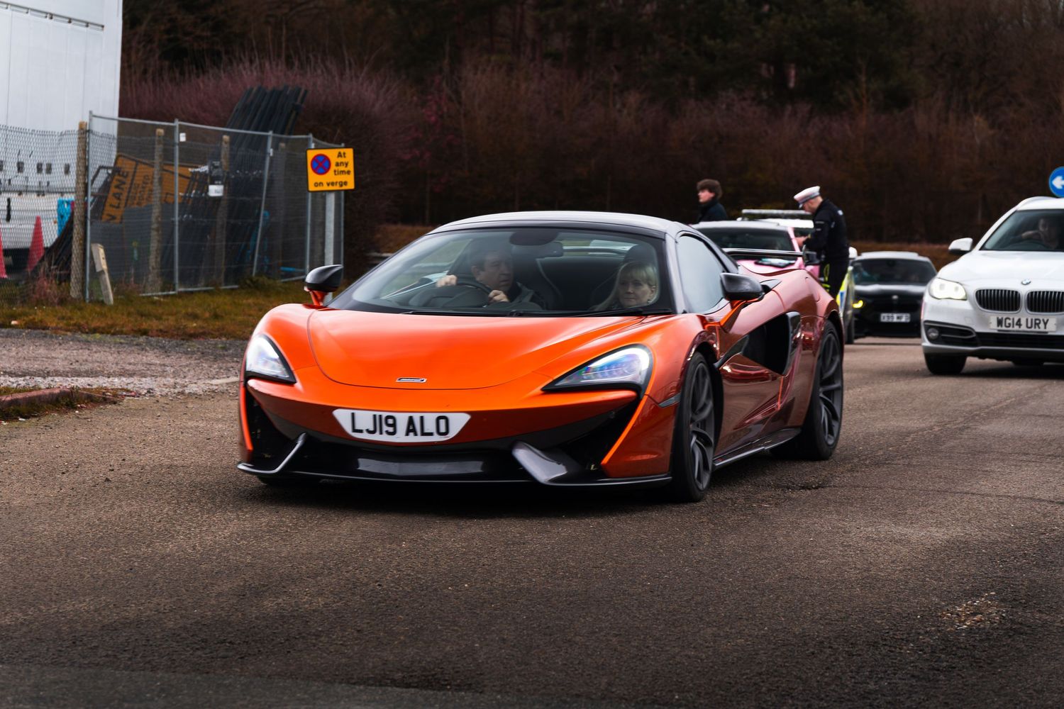 Orange McLaren 570S supercar with UK license plate driving at a car meet.
