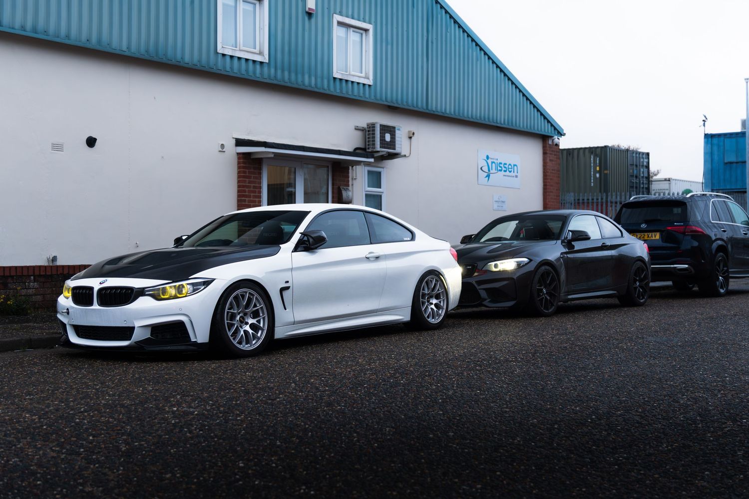 Two modified BMW 4 Series coupes parked outside an automotive workshop.