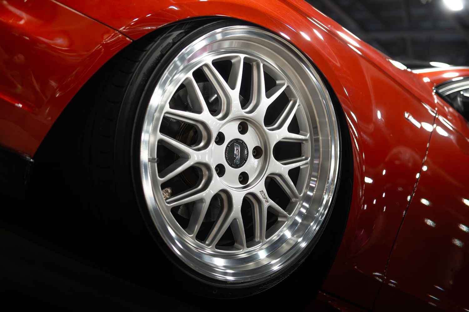 Close-up of a polished multi-spoke alloy wheel on a red sports car at an auto show.