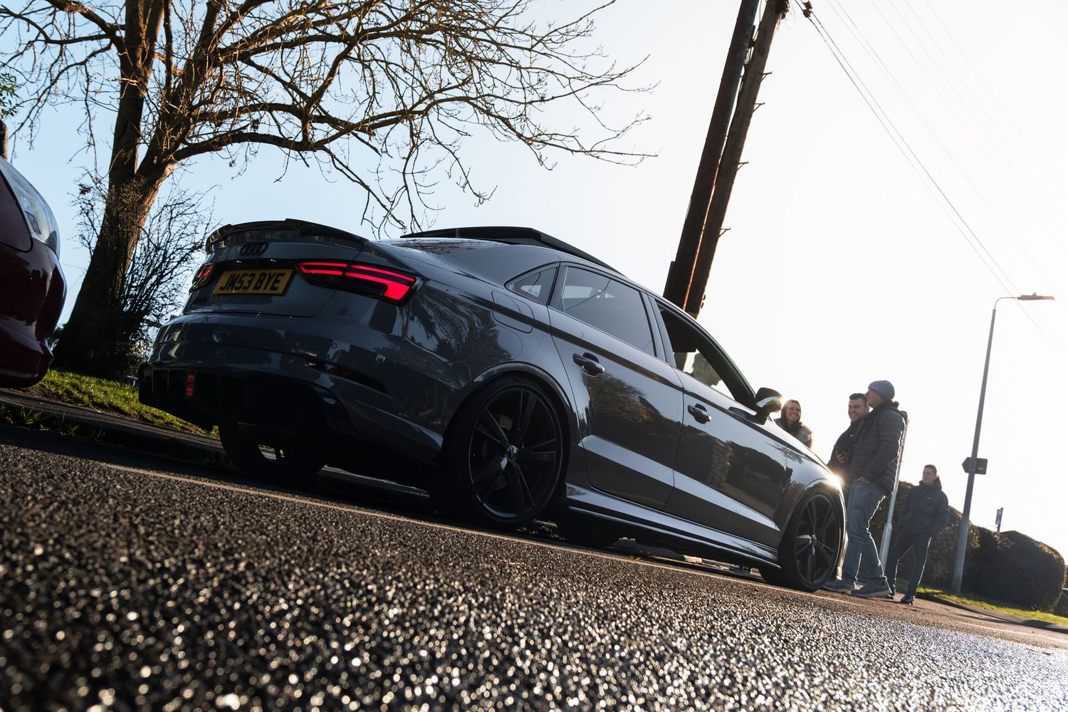Low angle rear view of a dark grey Audi RS3 parked on a residential street at a car meet.
