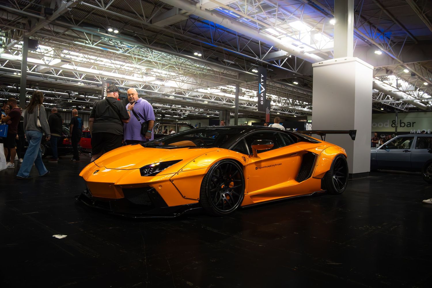 Orange Liberty Walk widebody Lamborghini Aventador on display at an indoor automotive show.