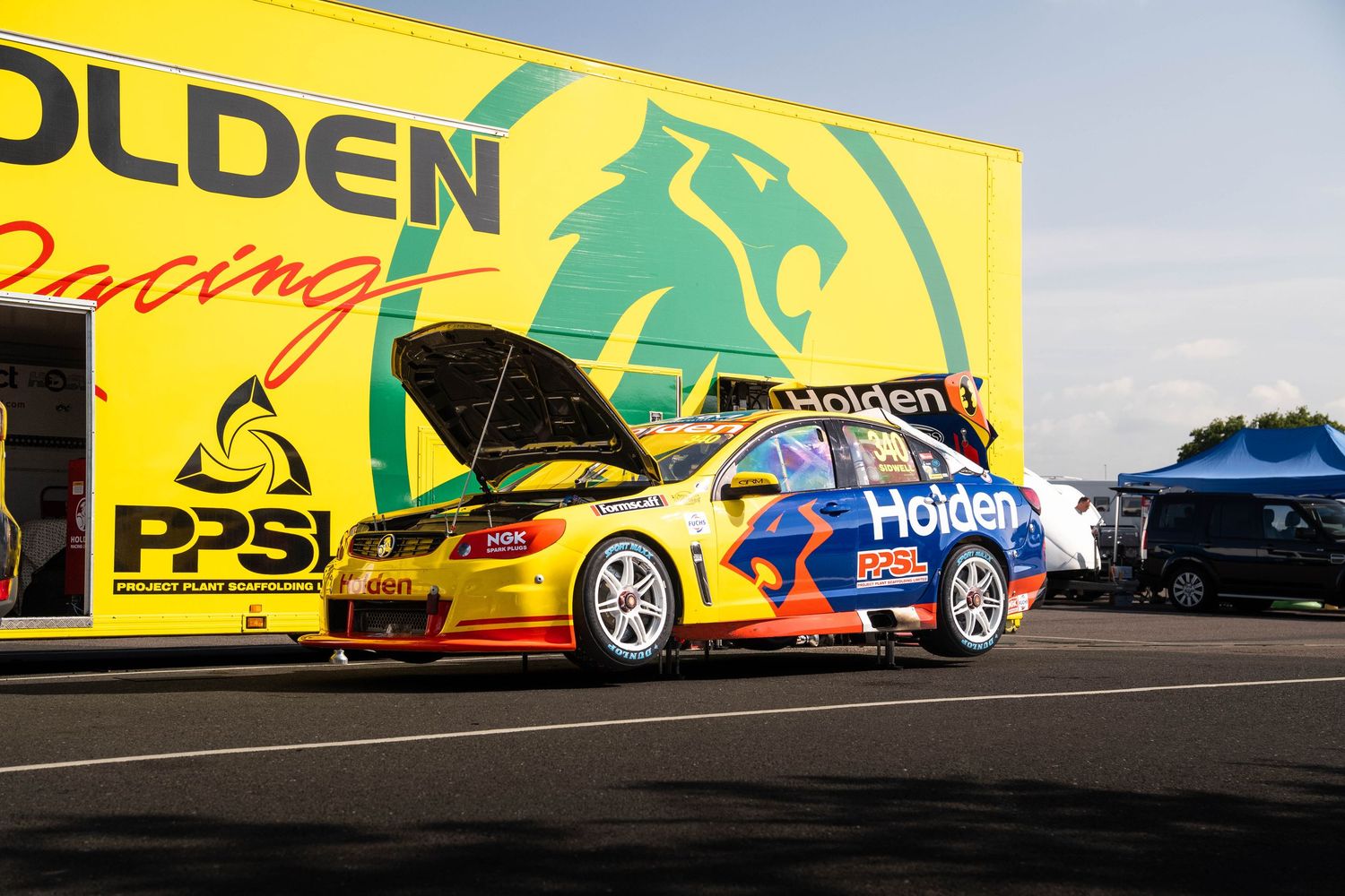 Holden Racing Team V8 Supercar with hood open in paddock at motorsport racing event.