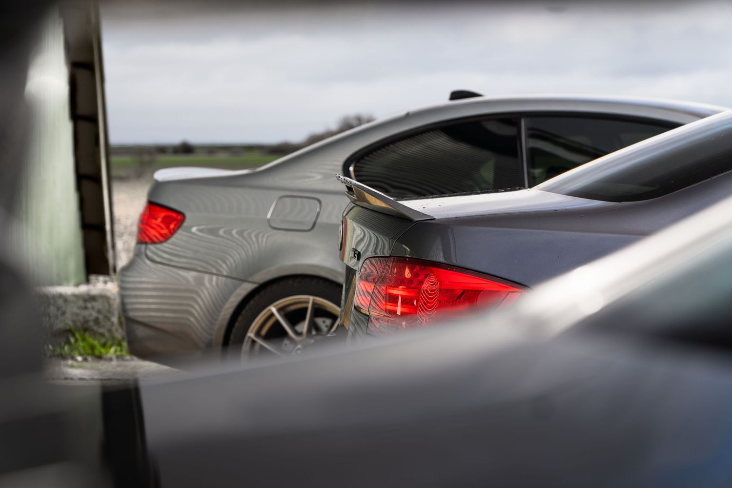 Rear view of a grey BMW M3 sedan with red taillights visible between other cars.
