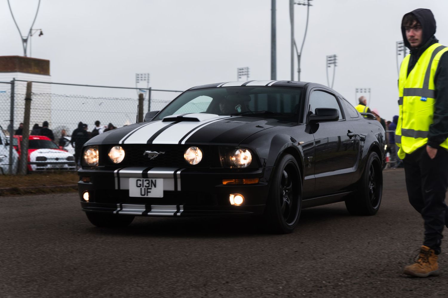 Black Ford Mustang Shelby GT with white racing stripes driving at a car show.