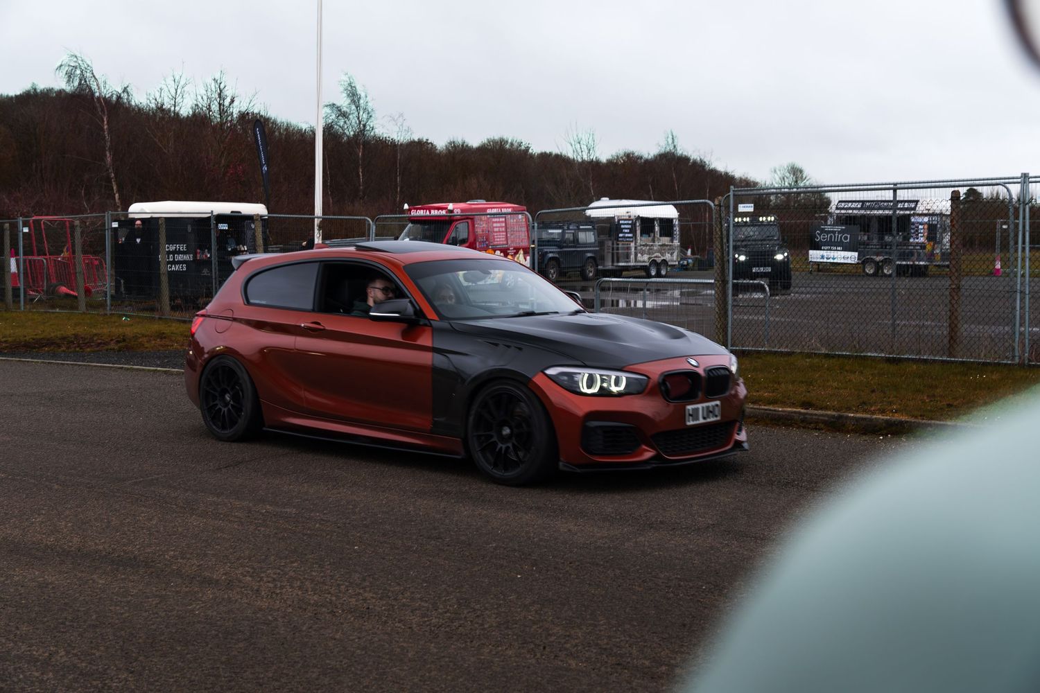 Modified red and black BMW 1 Series M135i on wet track at UK motorsport circuit on overcast day.