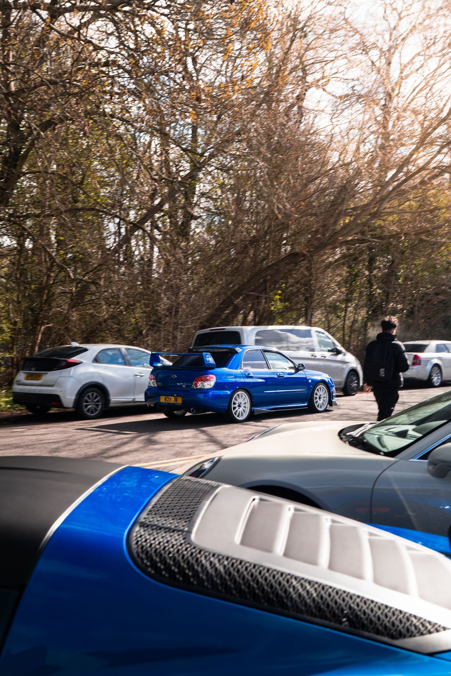 Blue Subaru Impreza WRX STI at outdoor car meet surrounded by trees.