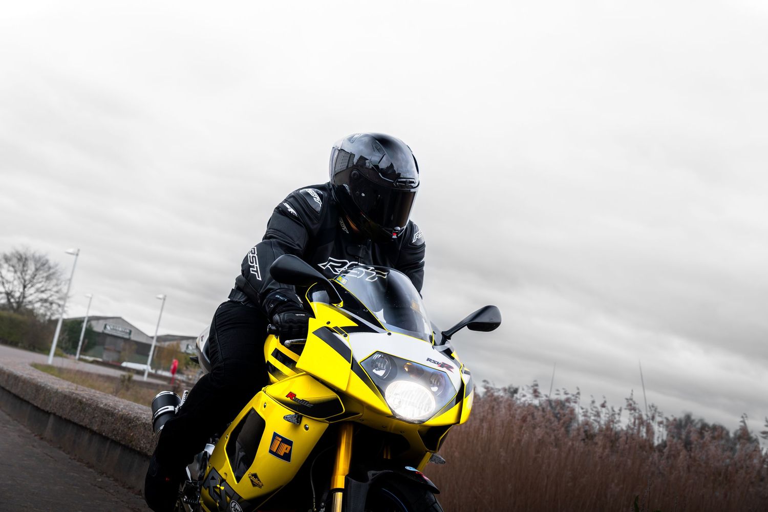 Low angle view of rider on yellow Aprilia RSV superbike under grey sky.